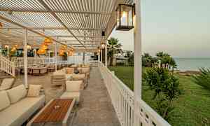 Utendørsområde med sittegrupper og utsikt over grønt område og hav. (AI-generert tekst)