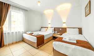 Hotellrom med to separate senger, lys innredning og et vindu med mørke gardiner. (AI-generert tekst)