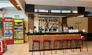 En bar med høye røde stoler og en opplyst bardisk. Bak er drikkevarer og shishaer. (AI-generert tekst)