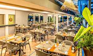 Et restaurantmiljø med bord og stoler klare, dekorert med planter og pent plasserte servietter. (AI-generert tekst)