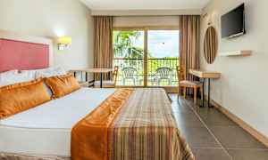 Interiør av et hotellrom med en stor seng, en balkong med utemøbler og en TV på veggen. (AI-generert tekst)