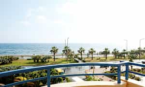 Utsikt fra en balkong mot en kystlinje med palmer og hav. (AI-generert tekst)