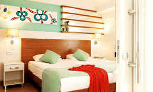 Rom med en dobbeltseng, to grønne puter, et rødt tekstil og veggdekorasjon. (AI-generert tekst)