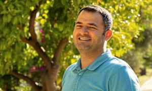 En person i en blå skjorte står foran en frodig hage. (AI-generert tekst)