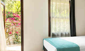 Et lyst rom med en seng og et åpent vindu som vender mot en frodig balkong med blomster. (AI-generert tekst)