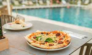 En pizza på et bord ved et basseng. (AI-generert tekst)