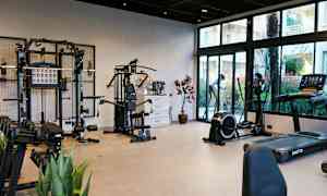 Et treningsstudio med ulike treningsapparater og vekter, samt glassvinduer som viser utsikten utenfor. (AI-generert tekst)