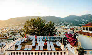 En terrasse med solsenger og parasoller samt utsikt over byen med fjell i bakgrunnen. (AI-generert tekst)