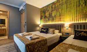 Et hotellrom med to senger, luftig dekorert med gylne aksenter og en vegg med moderne tekstur bak sengene. (AI-generert tekst)