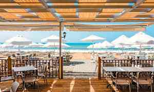 Utendørs servering med bord, stoler og parasoller nær sjøen. (AI-generert tekst)