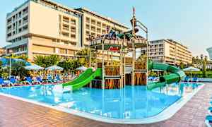 Utendørs bassengområde med en lekeplass med grønne sklir og et nærliggende hotell. (AI-generert tekst)