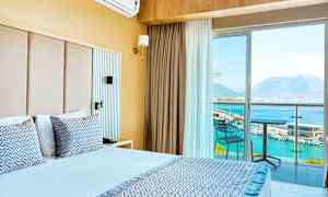Hotellrom med dobbeltseng, balkong med utsikt over havet og fjellene. (AI-generert tekst)