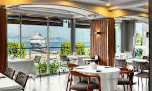 Restaurant med utsikt mot et cruiseskip ved en havn. (AI-generert tekst)