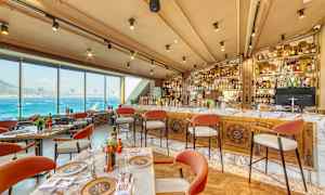 Restaurant med utsikt over havet, bord og stoler, samt en velutstyrt bar. (AI-generert tekst)