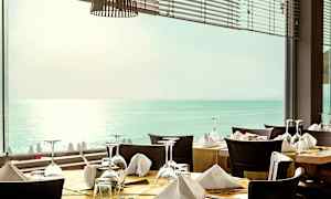 Restaurant med dekkede bord foran et vindu som har utsikt over havet. (AI-generert tekst)