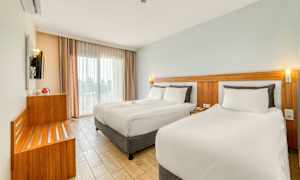 Moderne hotellrom med to senger, lyse farger og store vinduer. (AI-generert tekst)