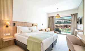 Hotellrom med dobbeltseng, sofa og utsikt mot et basseng. (AI-generert tekst)