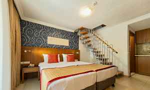 Et hotellrom med to senger, dekorativ tapet og en spiraltrapp som leder oppover. (AI-generert tekst)