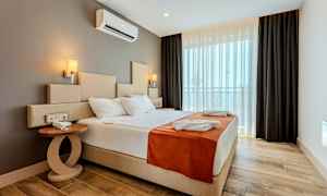 Et hotellrom med en stor seng, sidebord og vindu med mørkleggingsgardiner. (AI-generert tekst)