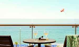 En balkong med bord, to glass og en bok med utsikt over havet. (AI-generert tekst)