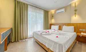 Hotellrom med en dobbeltseng redd opp med hvite laken og dekorert med blomster. (AI-generert tekst)