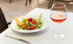 En tallerken med salat og et glass rosévin på et dekket bord. (AI-generert tekst)
