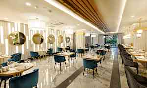 Bilde av en elegant restaurant med blå og svarte stoler, marmorgulv og gulldetaljer. (AI-generert tekst)