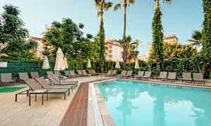 Utendørs svømmebasseng ved et hotell, omgitt av solsenger og parasoller. (AI-generert tekst)