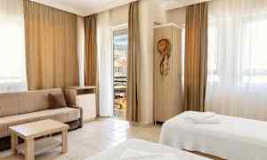 Et hotellrom med to senger, en sofa og balkongdør. (AI-generert tekst)