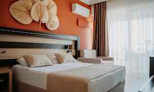 Hotellrom med oransje vegg, dobbeltseng med to puter og dekorative gjenstander over sengen. (AI-generert tekst)