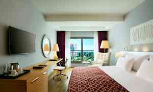 Et moderne hotellrom med en seng, skrivebord, lenestol og balkong med utsikt. (AI-generert tekst)