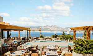 En restaurantterrasse med havutsikt og fjell i bakgrunnen. (AI-generert tekst)