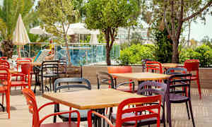 Fargerike stoler og bord plassert på en uteterrasse nær grøntområder og et basseng. (AI-generert tekst)