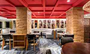 En restaurant med røde tak og trestolper samt grå sofaer og moderne spisebord. (AI-generert tekst)