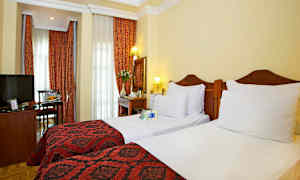 Hotellrom med to enkeltsenger, røde dekorasjoner og gardiner. (AI-generert tekst)