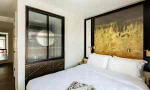 Hotellrom med en stor seng, aviser på sengen og en dekorativ vegg. (AI-generert tekst)