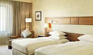 Et hotellrom med to enkeltsenger, en sitteplass med pute og et vindu med gardiner. (AI-generert tekst)