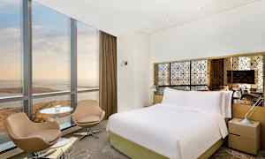 Bilde av et hotellrom med stor seng, to stoler, bord og vindu med utsikt. (AI-generert tekst)