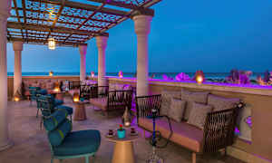 En overbygd terrasse med sittemøbler og belysning, med utsikt over havet om kvelden. (AI-generert tekst)