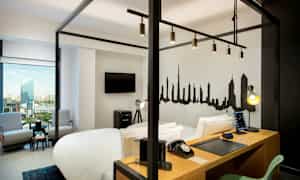 Et moderne hotellrom med en himmelseng, arbeidsbord, TV, sittegruppe og en bysilhuett malt på veggen. (AI-generert tekst)