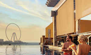 Personer står i et basseng med utsikt mot et stort pariserhjul ved solnedgang. (AI-generert tekst)