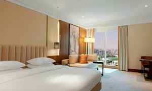 Et hotellrom med en dobbeltseng, sittegruppe og et stort vindu med utsikt over byen. (AI-generert tekst)