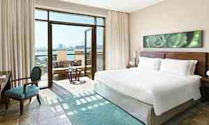 Moderne hotellrom med en stor king size-seng, en sittegruppe og åpen balkong med havutsikt. (AI-generert tekst)