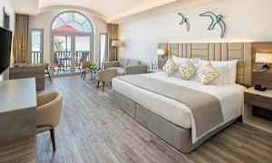 Et moderne hotellrom med en bred seng, sofa og skrivebord. Stort vindu og balkong i bakgrunnen. (AI-generert tekst)