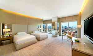 To enkeltsenger i et moderne hotellrom med store vinduer og byutsikt. (AI-generert tekst)