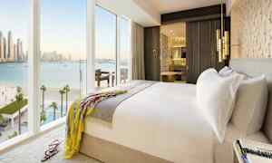 Et lyst hotellrom med en dobbeltseng, et åpent bad og store vinduer som viser utsikt over havet. (AI-generert tekst)