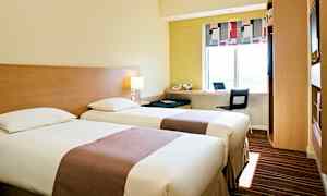 Et hotellrom med to enkeltsenger, en arbeidsstasjon ved et vindu og moderne møbler. (AI-generert tekst)