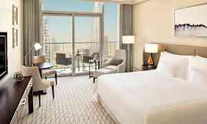 Et moderne hotellrom med en stor seng, sittegruppe og en balkong med utsikt over en stor by. (AI-generert tekst)