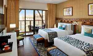 To oppredde senger i et hotellrom med moderne innredning, store vinduer med balkong og utsikt. (AI-generert tekst)