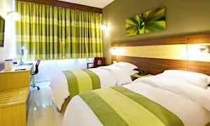 Et hotellrom med to enkeltsenger, skjult belysning ved sengegavlene, et skrivebord og grønne gardiner som komplementerer rommets innredning. (AI-generert tekst)